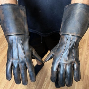 May include: A pair of brown leather gloves with a distressed look. The gloves have a long cuff and are made of a soft, supple leather.