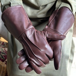 May include: A pair of brown leather gloves with a long cuff. The gloves are folded in half and the fingers are interlocked.