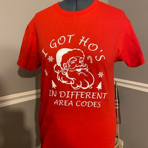 May include: Red t-shirt with a white graphic of Santa Claus and the text "I got Ho's in different area codes".
