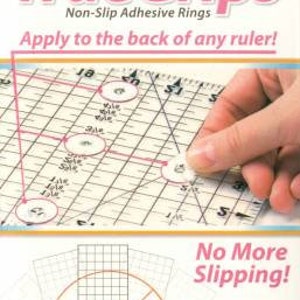 Pode incluir: Um pacote de anéis adesivos antiderrapantes TrueGrips para réguas. O pacote contém 15 anéis grandes e 15 pequenos. A imagem mostra uma mão colocando um anel em uma régua. O texto "No More Slipping!" está impresso na embalagem.