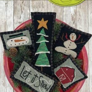 May include: Five punch needle bowl fillers with a winter theme. The set includes a snowman, a Christmas tree, a house, and two pieces with the text "Let it Snow".