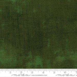 May include: Dark green fabric with a textured, mottled appearance. The fabric has a distressed look with darker green and black accents, and a ruler is at the bottom.