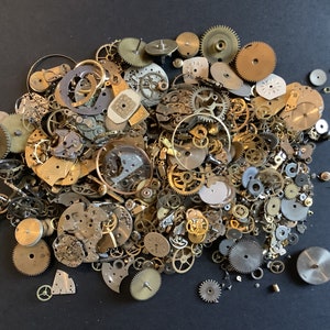 May include: A large collection of assorted watch parts and gears in gold and silver tones. The parts are scattered on a black surface.