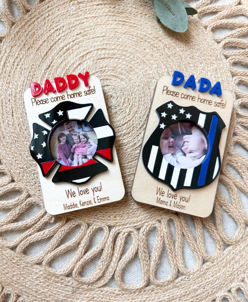 May include: Two wooden photo frames with the words "DADDY" and "DADA" in red and blue, respectively. Each frame has a circular photo opening and the text "Please come home safe!" and "We love you!" with names. One frame is shaped like a firefighter's emblem.