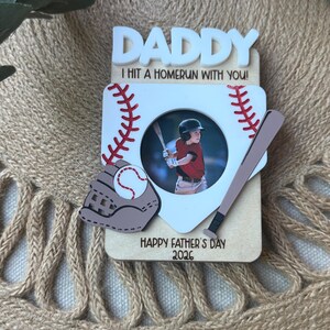 May include: A baseball-themed photo frame with the word "DADDY" in white block letters. The frame includes a baseball, bat, and glove, with the text "I HIT A HOMERUN WITH YOU!" and "HAPPY FATHER'S DAY 2026". A photo of a child playing baseball is in the center.