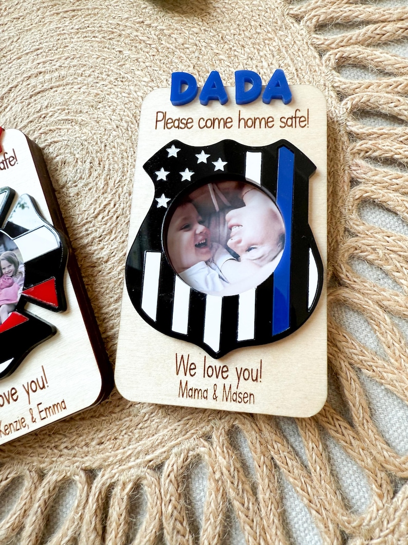 May include: Wooden photo frame with a police badge design. The frame has the word "DADA" in blue letters at the top, with the message "Please come home safe!" below. The frame includes a photo of two children and the message "We love you! Mama & Masen."