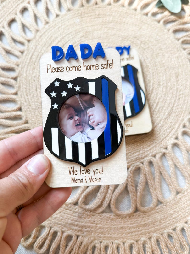 May include: Wooden photo frame with a police badge design. The frame has the word "DADA" in blue letters at the top, with the message "Please come home safe!" below. The frame includes a photo and the words "We love you! Mama & Masen."