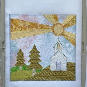 Puede incluir: Un bordado de aplique de tela cuadrado que presenta una iglesia blanca con campanario, dos pinos verdes y un sol amarillo con rayos radiantes. El fondo consiste en una tela jaspeada de color azul claro y rosa con puntadas de acolchado.