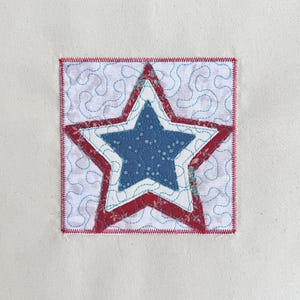 May include: A square fabric patch with a blue star, white dots, and red and white star design. The star is centered on a white background with blue swirling stitch details, framed by a red stitched border.