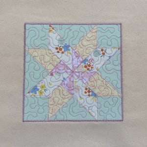 以下が含まれることがあります： ピンク、イエロー、ブルーの色の星形のデザインが施されたキルティングされた布の正方形。星は、渦巻き模様のライトブルーの背景で囲まれています。