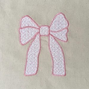 Może przedstawiać: Różowa kokardka z ozdobnym, wirującym wzorem. Kokardka jest przyszyta do naturalnego materiału.