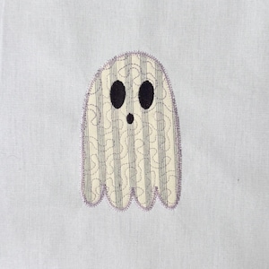 Peut inclure: Une applique fantôme brodée sur un fond en tissu blanc. Le fantôme présente un corps couleur crème avec des rayures grises verticales et un motif de points en tourbillon. Il possède deux grands yeux ovales noirs et une petite bouche ronde noire.