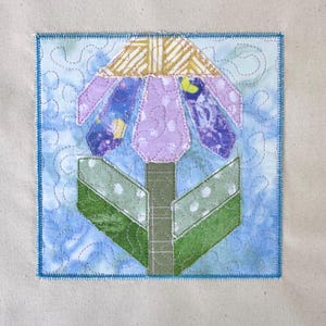 Può includere: Applicazione floreale in tessuto fatta a mano con sfondo azzurro e bordo blu. Il fiore ha una parte superiore a righe oro e bianche, petali viola e foglie verdi con pois bianchi. Il disegno è cucito con filo d'argento.