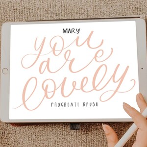 Pu&ograve; includere: Un tablet digitale che mostra un design di calligrafia rosa che dice "you are lovely" con il testo "Procreate Brush" sotto. Il tablet &egrave; su una superficie marrone testurizzata.