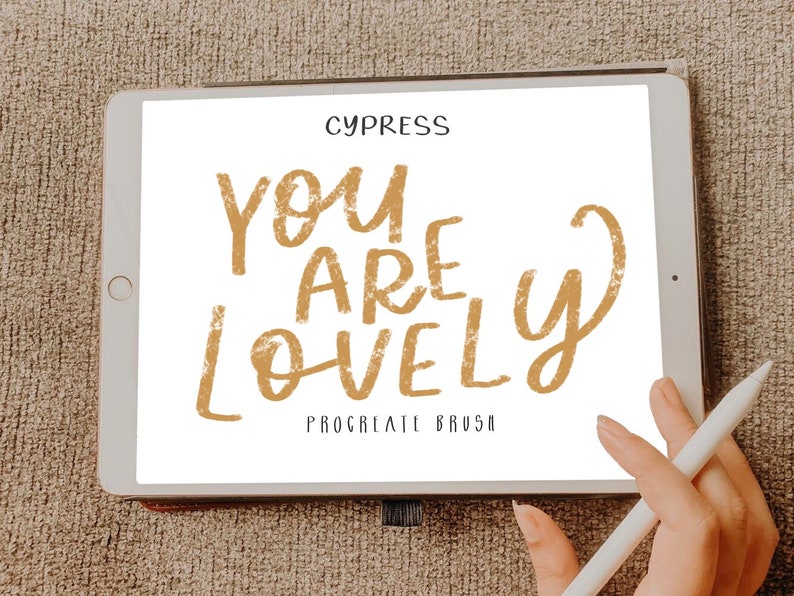Pu&ograve; includere: Uno schermo di tablet digitale che mostra il testo "You are lovely" in un carattere dorato testurizzato. Il testo &egrave; scritto in uno stile informale, a mano libera. Le parole "Procreate Brush" sono scritte in un carattere pi&ugrave; piccolo sotto il testo principale.