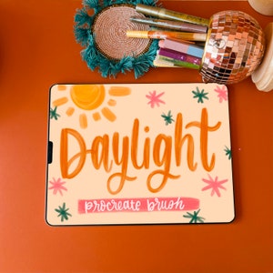 Op de afbeelding: Een digitale illustratie van het woord "Daylight" in een heldere oranje kleur met een zon en sterren op de achtergrond. De tekst "procreate brush" staat in een kleiner lettertype onder het woord "Daylight".