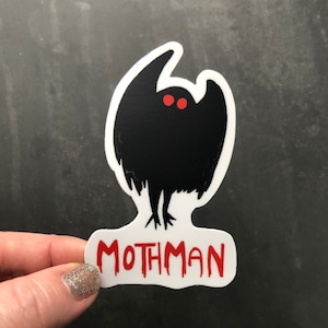 May include: A white sticker with a black silhouette of a mothman with red eyes and the text "MOTHMAN" in red.