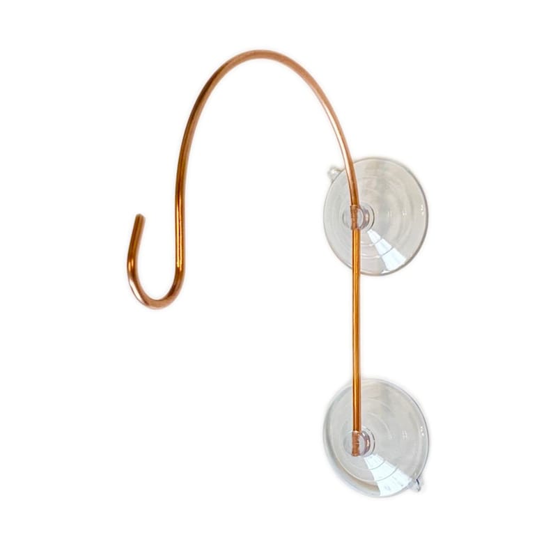 May include: A copper-colored, curved hook with a suction cup base. The hook is designed to hang items and attaches to smooth surfaces. The suction cups are clear and round, providing a secure hold. The hook is made of a durable metal.