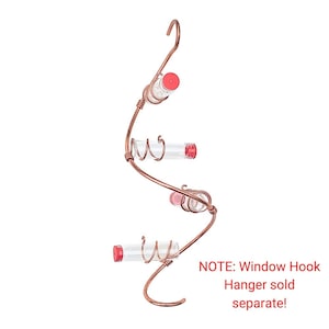 May include: Copper-colored hummingbird feeder with three clear glass tubes and red caps. The feeder has a curved, spiral design with a hook at the top for hanging. The text on the image says "NOTE: Window Hook Hanger sold separate!"