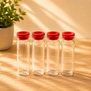 May include: Four clear glass vials arranged in a row, each featuring a cylindrical body and a bright red plastic cap. The vials are transparent, empty, and have a smooth, uniform design with a slightly flared rim at the top of each glass neck.
