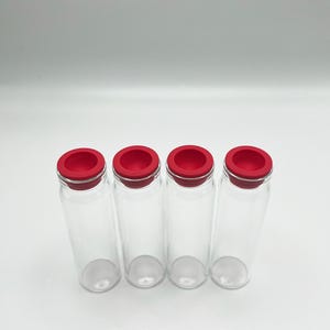May include: Four clear glass vials arranged in a row, each featuring a bright red circular silicone stopper. The vials are cylindrical with a smooth, transparent body and a flat base, standing upright against a plain, neutral background.