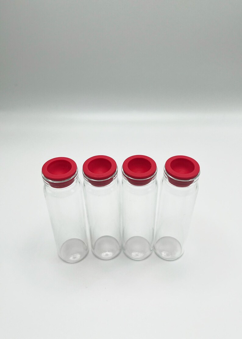 May include: Four clear glass vials arranged in a row, each featuring a bright red circular silicone stopper. The vials are cylindrical with a smooth, transparent body and a flat base, standing upright against a plain, neutral background.