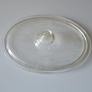 May include: Clear glass oval lid with a central knob. The lid features a delicate etched floral pattern. The transparent design allows a clear view of the contents. A classic kitchenware item.