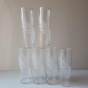May include: Six clear, tall drinking glasses. Each glass features a white, etched leaf design. The glasses are arranged in a pyramid shape, with three glasses on the bottom, two in the middle, and one on top.