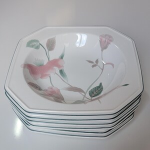 May include: A stack of white octagonal bowls with a floral design. Each bowl features a pink and green floral pattern and a thin green border. The bowls are stacked on top of each other.