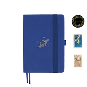 Könnte beinhalten: Ein blaues Notizbuch mit einem goldenen Planeten- und Sternen-Design. Das Notizbuch hat einen blauen Gummizugverschluss und ein blaues Lesezeichenband.