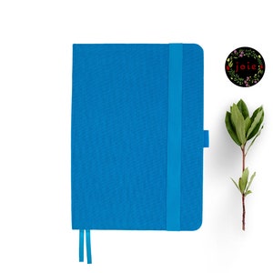 May include: A blue notebook with a matching elastic closure and a ribbon bookmark. The notebook is on a white background.