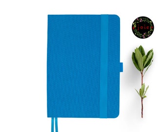 May include: A blue notebook with a matching elastic closure and a ribbon bookmark. The notebook is on a white background.