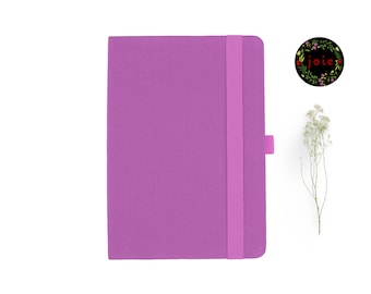 May include: A purple notebook with a pink elastic closure and a pink bookmark. The notebook has a textured cover.
