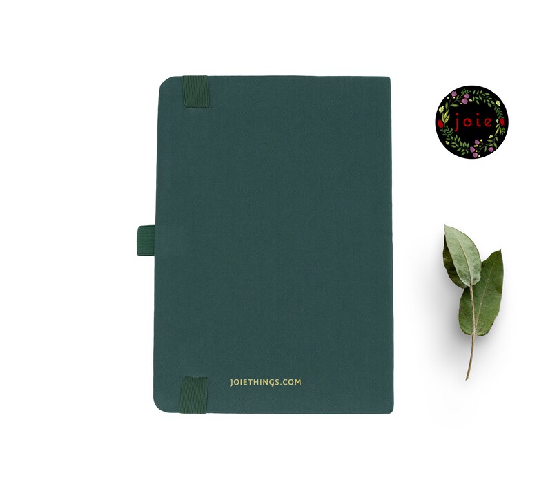 May include: A dark green notebook with a black elastic band closure and a gold inscription that reads "JOIETTHINGS.COM".