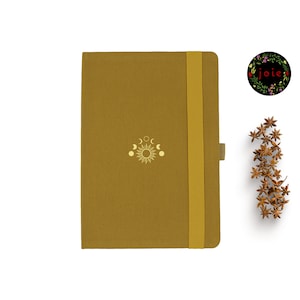 May include: A mustard yellow notebook with a gold sun and moon design and a yellow elastic closure. The notebook is closed.