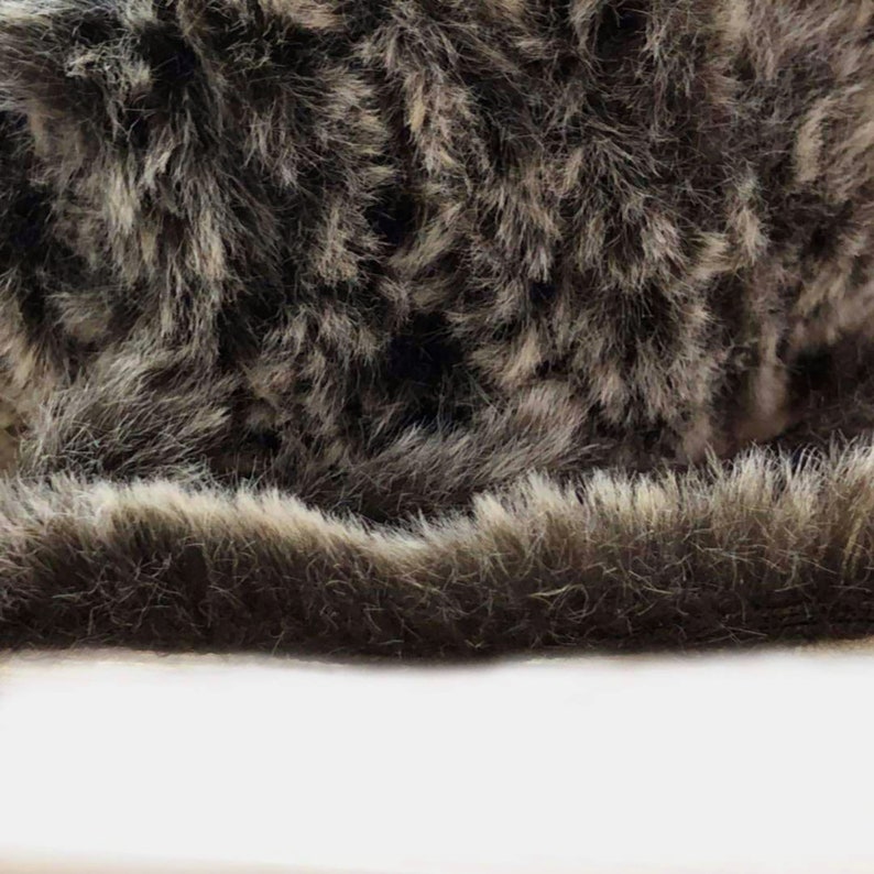 May include: Close-up of a soft, plush, brown and white faux fur fabric. The fur is very dense and fluffy, with a slight sheen.