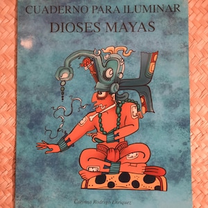 May include: A book titled "CUADERNO PARA ILUMINAR DIOSES MAYAS" features a colorful illustration of a Mayan deity. The cover is a teal blue with the illustration in orange, green, and black. The author's name, Corinna Rodrigo Enriquez, is at the bottom.
