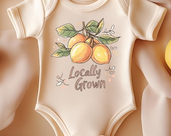 May include: A cream-colored baby onesie with a lemon graphic and the text "Locally Grown." The onesie is surrounded by fresh lemons and green leaves on a beige fabric background. The lemons are a bright yellow color.