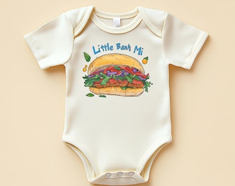 May include: Cream-colored baby bodysuit with a graphic of a Banh Mi sandwich. The sandwich illustration features a yellow bun, red and green vegetables, and the text "Little Banh Mi" in blue. The bodysuit has short sleeves and snap closures.