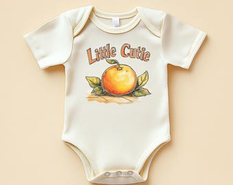 May include: A cream-coloured baby bodysuit with short sleeves and popper fastenings. It displays an orange graphic with green leaves and the text "Little Cutie" in orange. The garment is designed for infants.