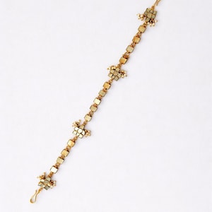 May include: A delicate gold-toned headpiece with a linear design. It features small, square-shaped embellishments and floral clusters, accented with tiny white beads. The headpiece has a hook at each end for secure placement.