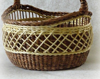 May include: A woven basket with a brown handle and a light brown and dark brown woven pattern. The basket is oval shaped and has a wide opening.