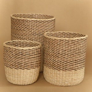 May include: A set of three cylindrical woven baskets featuring a two-tone design. The upper sections are constructed from dark brown twisted fibers, while the lower sections are made from light beige natural fibers, creating a distinct contrast.