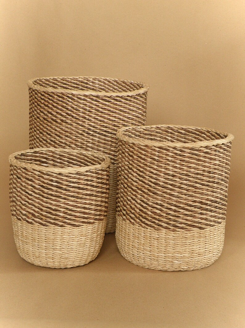 May include: A set of three cylindrical woven baskets featuring a two-tone design. The upper sections are constructed from dark brown twisted fibers, while the lower sections are made from light beige natural fibers, creating a distinct contrast.