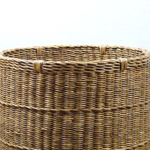 Op de afbeelding: Een geweven rieten mand met een ronde bovenkant en een natuurlijke bruine kleur.