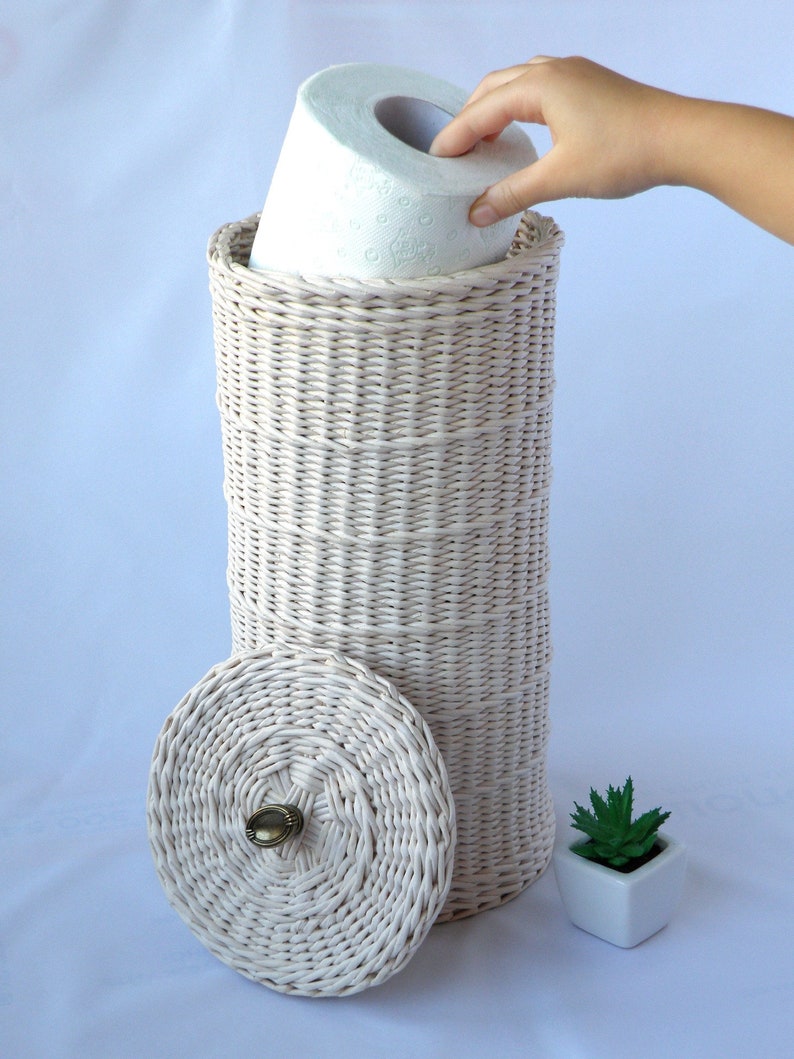 Puede incluir: Porta rollo de papel higi&eacute;nico de mimbre blanco con tapa y un rollo de papel higi&eacute;nico dentro. El porta rollo tiene un pomo de lat&oacute;n en la tapa.