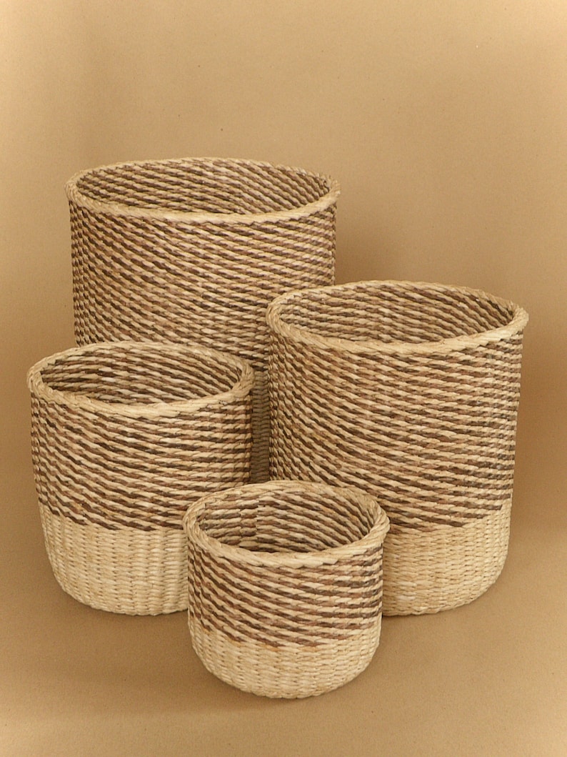 May include: A set of four cylindrical baskets of varying sizes, each featuring a two-tone design with a light beige woven base and a darker brown twisted rope pattern on the upper section, creating a textured appearance for storage.