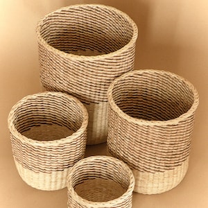 May include: A set of four cylindrical woven baskets of varying sizes. Each basket features a two-tone design with a natural light beige base and a darker brown woven upper section, creating a distinct horizontal color contrast throughout the set.