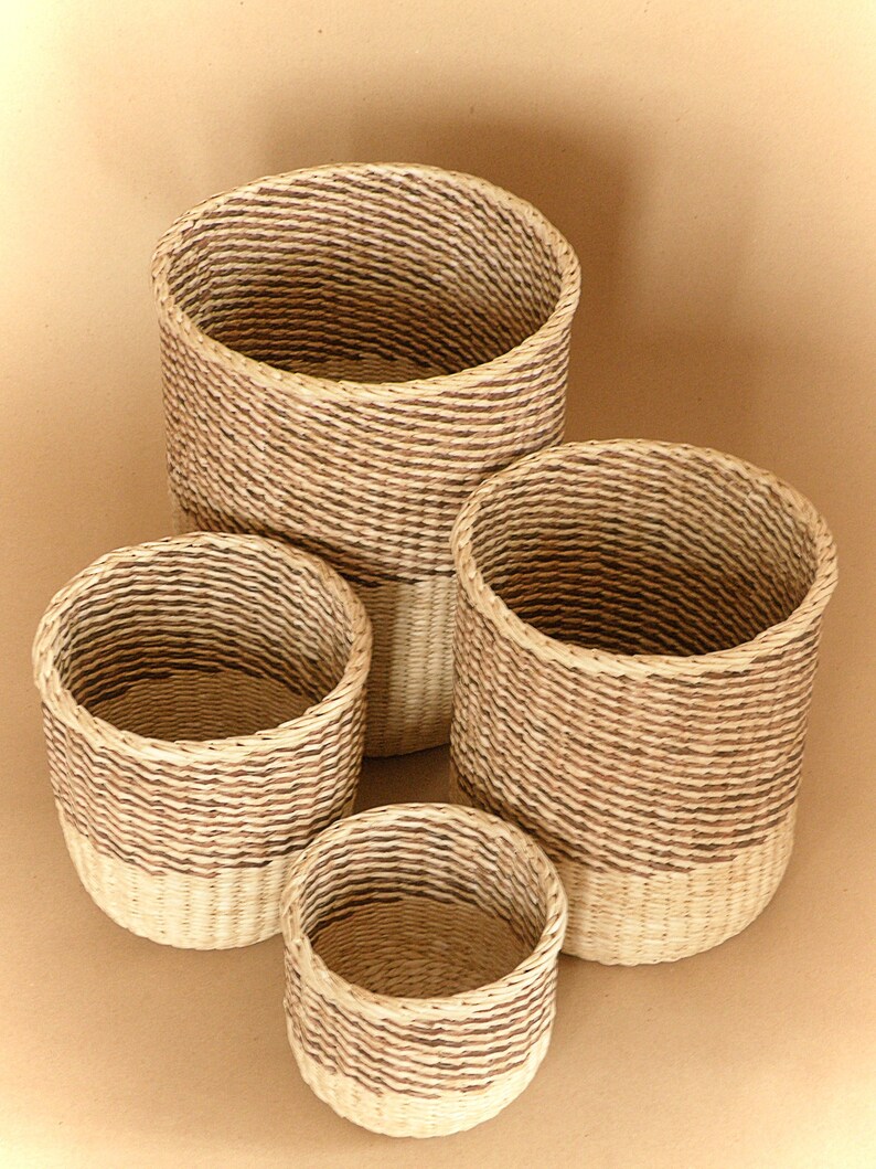 May include: A set of four cylindrical woven baskets of varying sizes. Each basket features a two-tone design with a natural light beige base and a darker brown woven upper section, creating a distinct horizontal color contrast throughout the set.