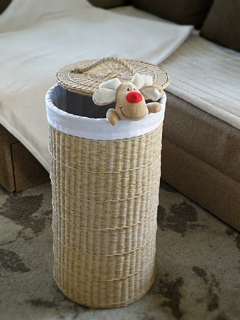 May include: A woven wicker laundry hamper with a white fabric liner and a removable lid. A plush reindeer toy is peeking out of the top of the hamper.